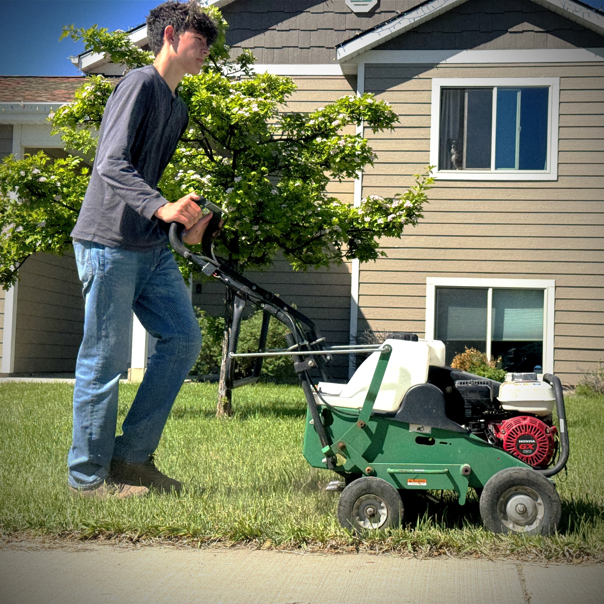 A square photo with the aerator front and center with one of the teens pushing it to aerate a lawn in Kalispell